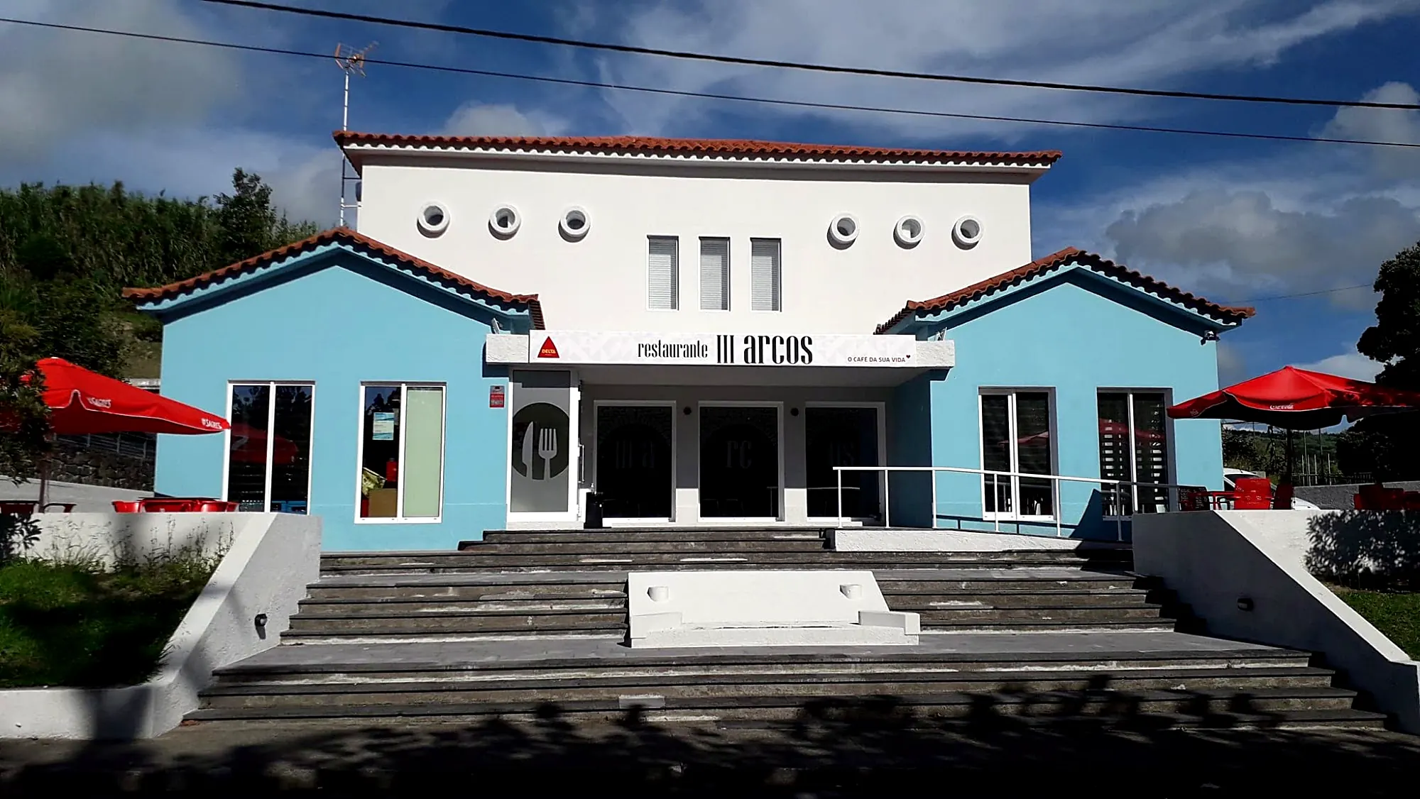 Fachada do Restaurante III Arcos, edifício branco e azul com escadaria, em Ginetes